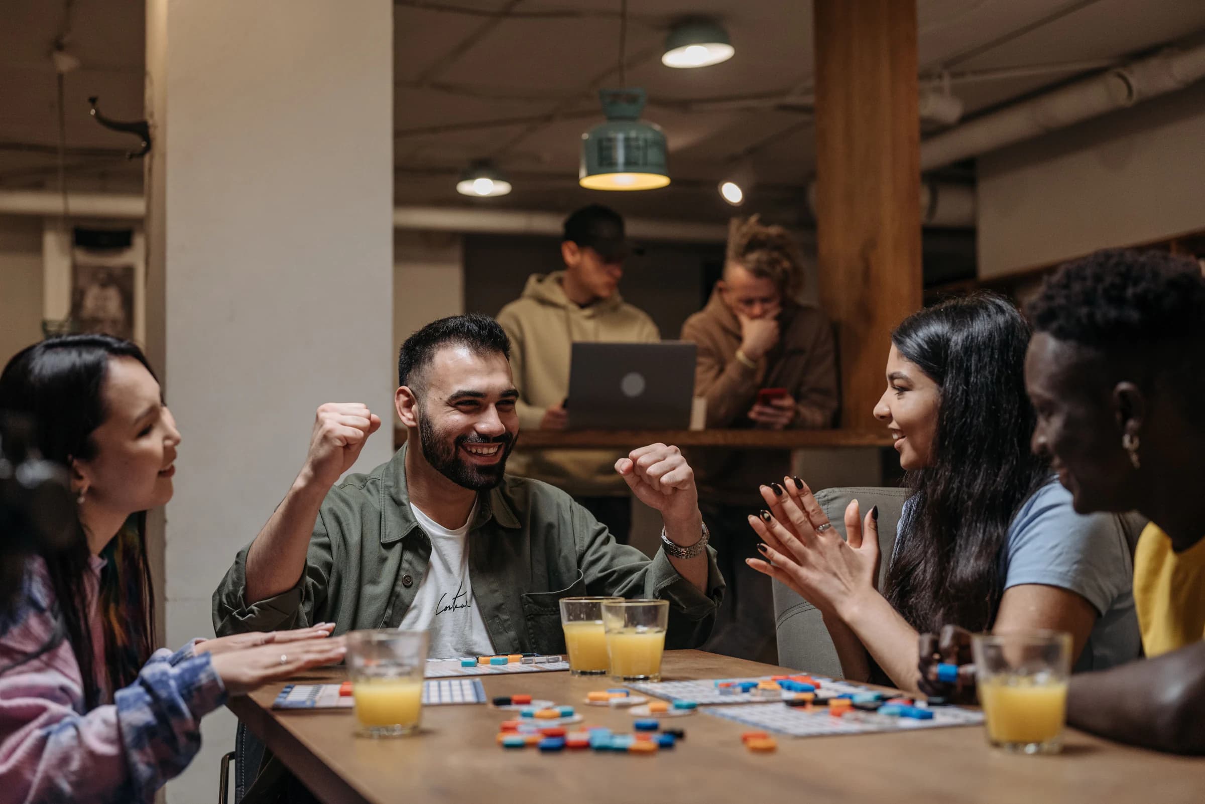 Amigos rindo e comemorando em volta de uma mesa durante uma partida de jogo de tabuleiro
